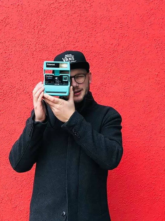 David s Polaroidem u oka před červenou zdí